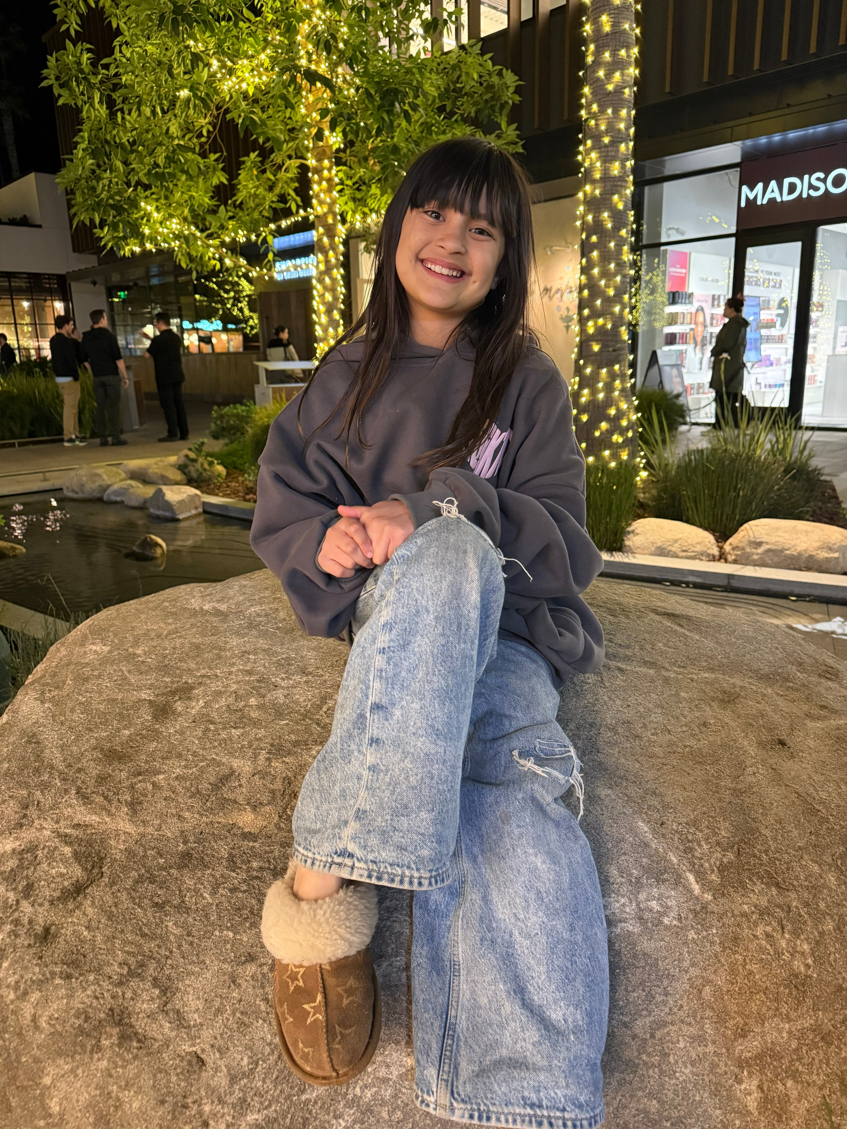 Girl sitting on rock at outdoor mall with fairy lights